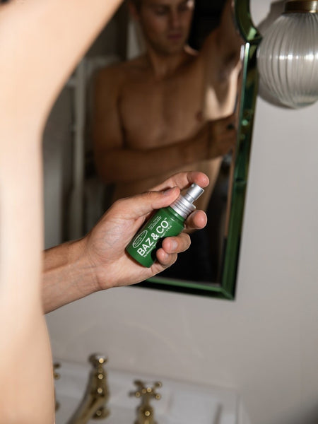Baz & Co Skincare green spray deodorant bottle held by a man in a bathroom, 50ml aluminium-free formula.