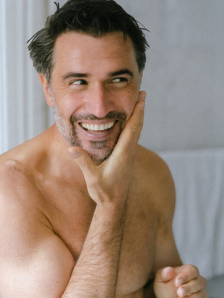 Baz & Co Skincare man with clean skin, smiling and touching his face, showing smooth, balanced complexion.